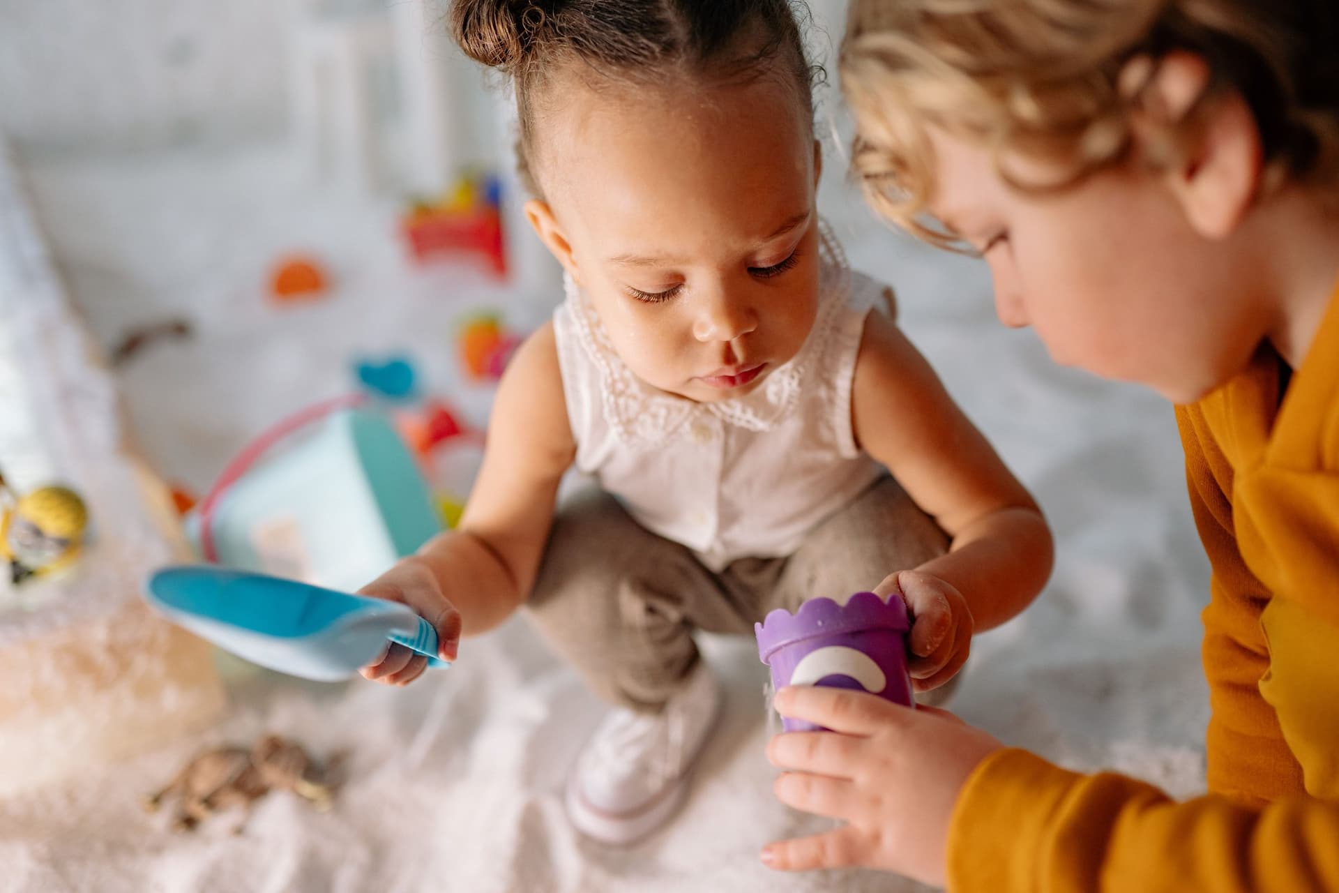 Two young children playing together with a toy spade and a sand mould