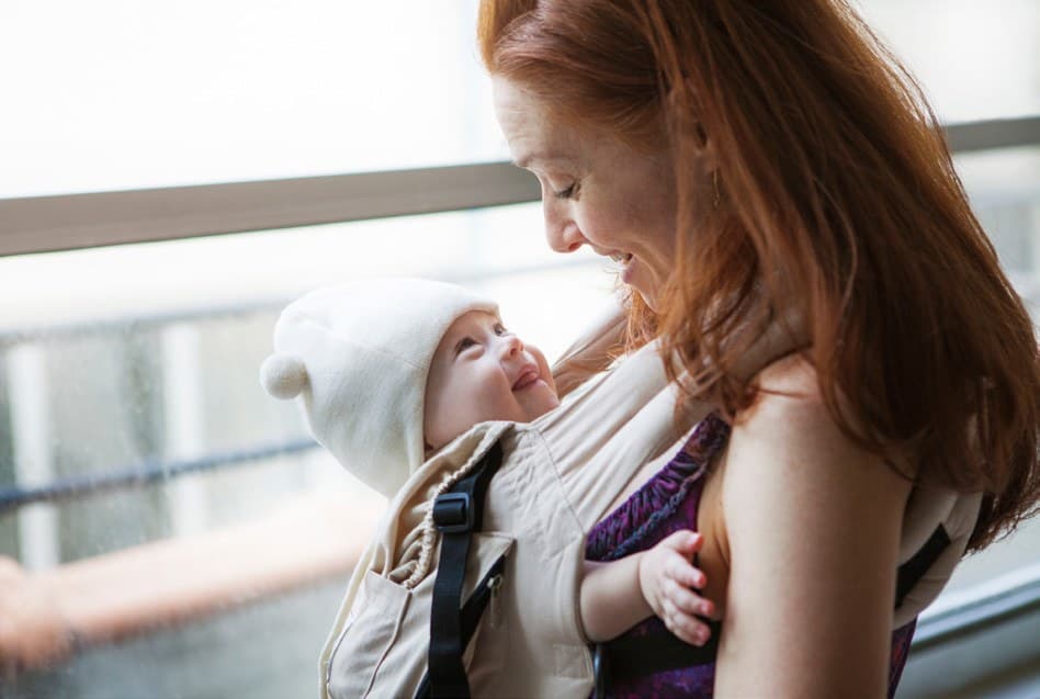 A mother smiling down at her baby, carried close in a sling